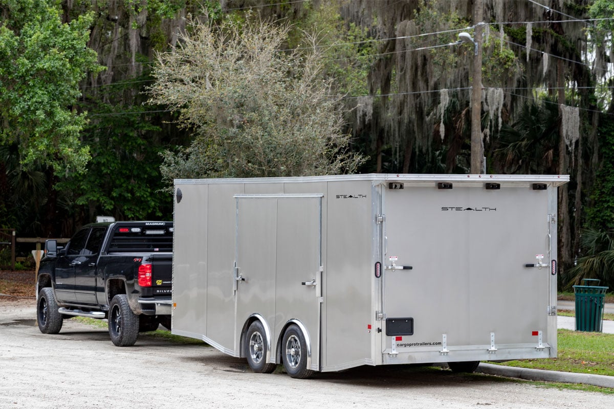 Black Truck Hauling Enclosed Supreme Car Hauler Trailer On Dirt Road