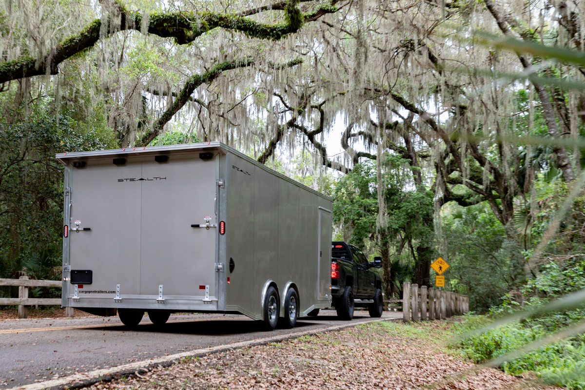 Black Truck Hauling Enclosed Supreme Car Hauler Trailer On Main Road