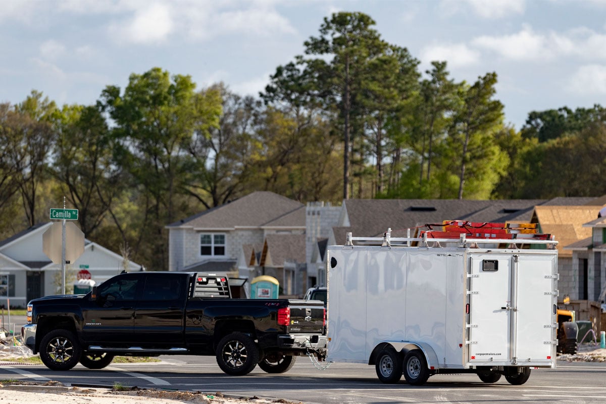 Black Truck Hauling White Enclosed Ultimate Contractor Package Trailer Through Construction Site