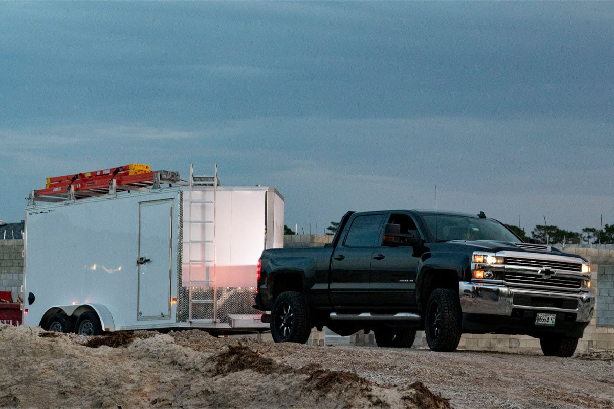 Black Truck Towing White Enclosed Ultimate Contractor Package Trailer On Dirt Road