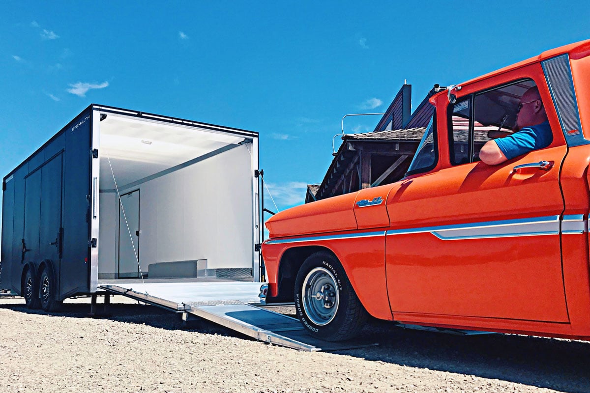 Orange Car Pulling Out Of Gray Enclosed Car Hauler Trailer