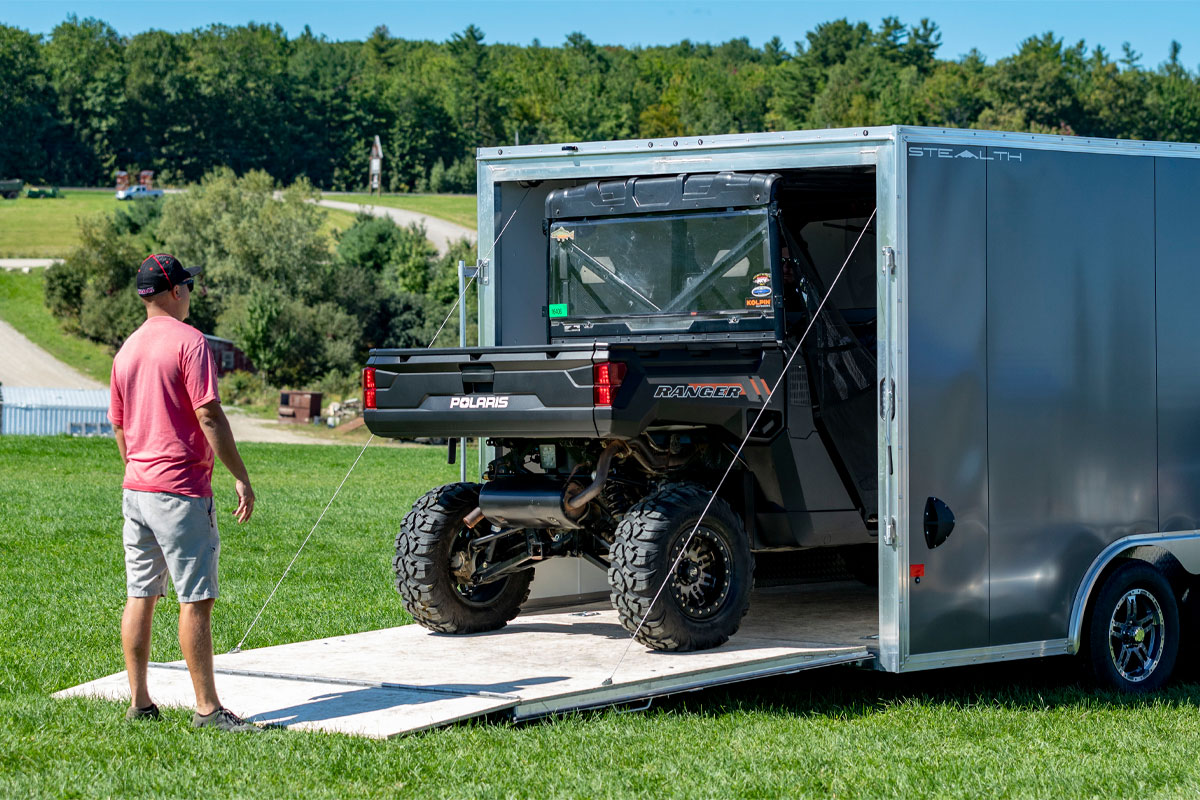 Person Loading ATV Into Gray Enclosed Car Hauler Trailer