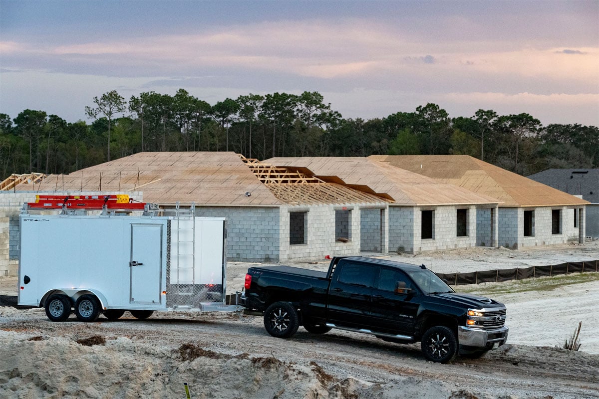 Side View Of Black Truck Hauling White Enclosed Ultimate Contractor Package Trailer Through Site