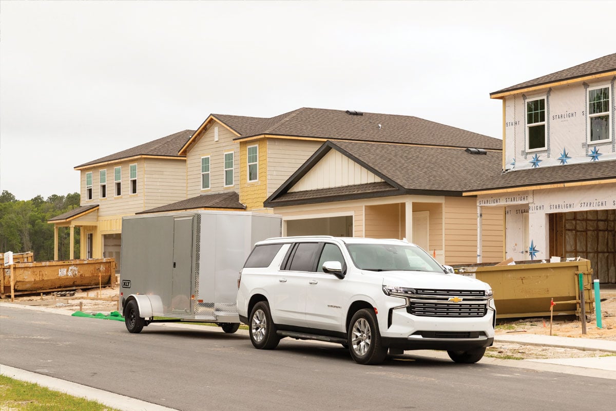 White SUV towing gray trailer in front of house construction