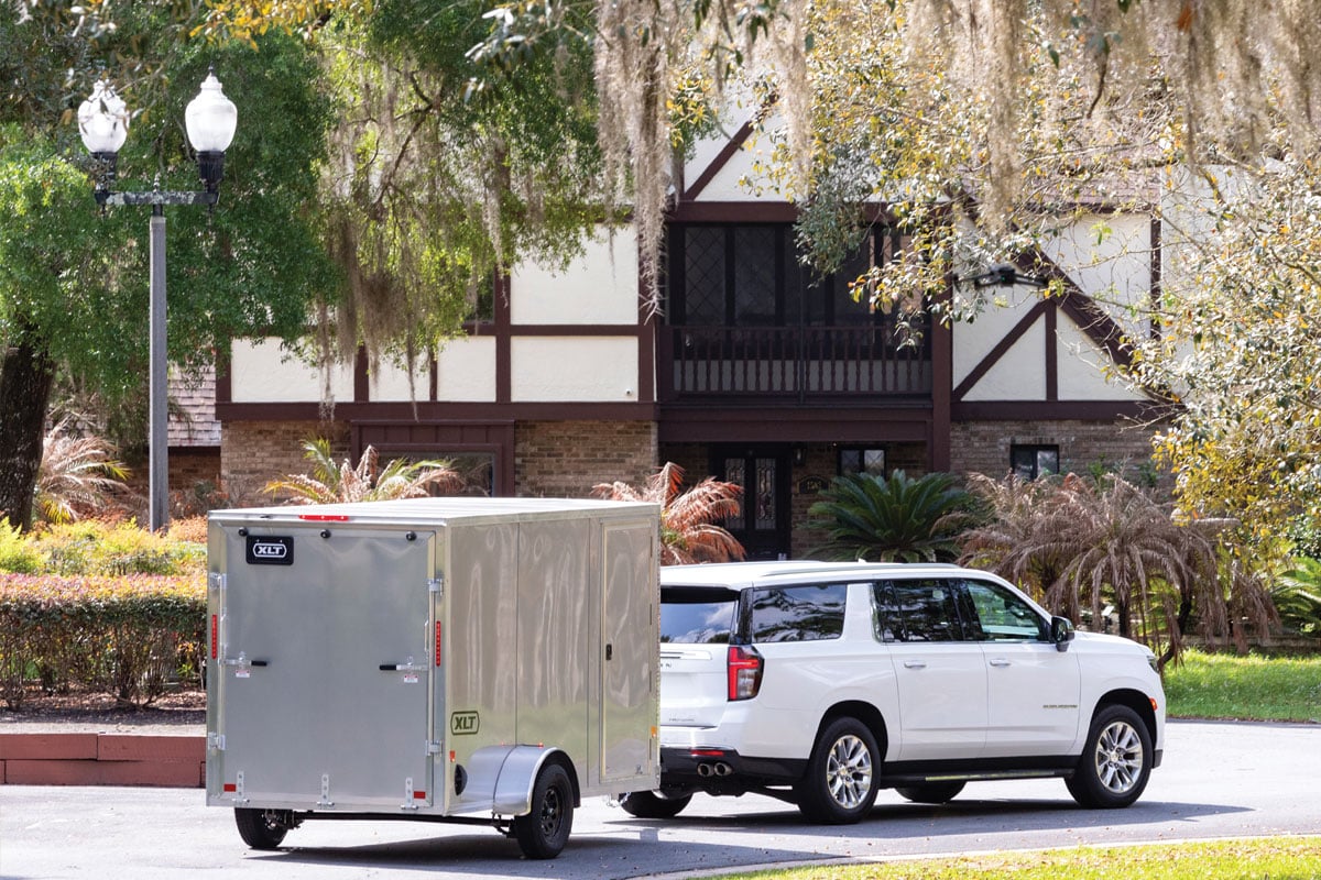White SUV towing gray trailer in front of house